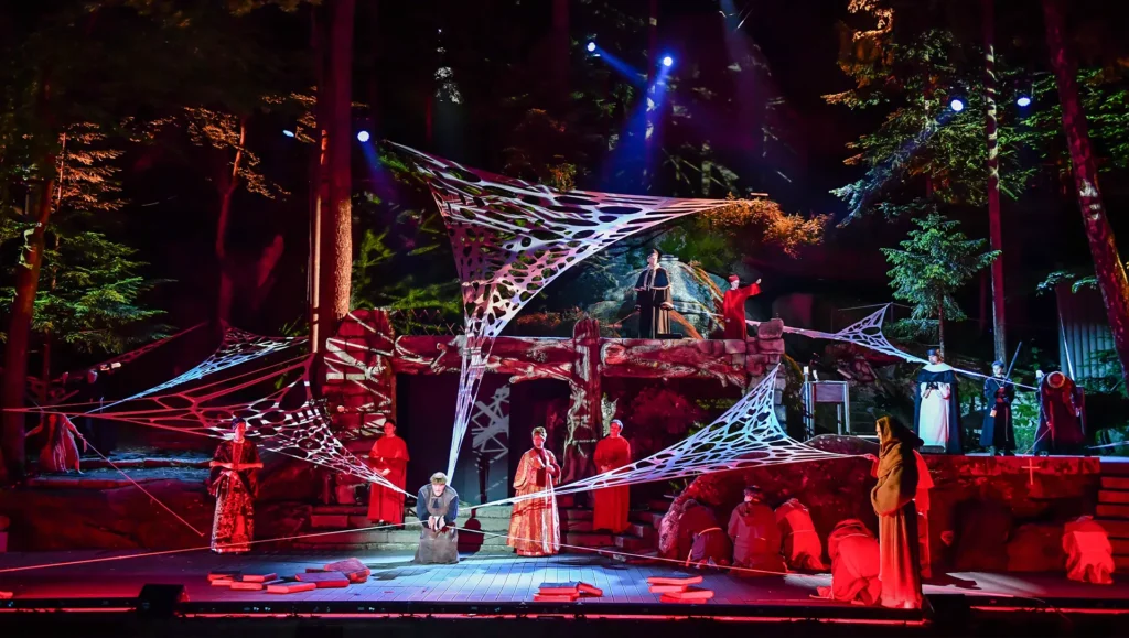 Bunt erleuchtete Bühne bei Nacht, mit Person im Zentrum und Spinnweben